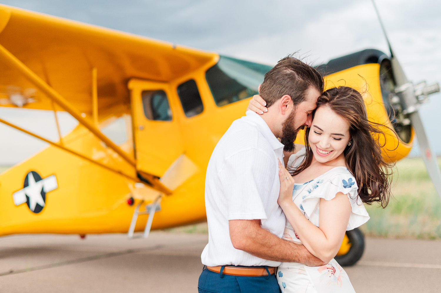 A man and woman pose in front of a yellow airplane during their engagement photos at the Platte Valley Airport in Fort Lupton, Colorado.