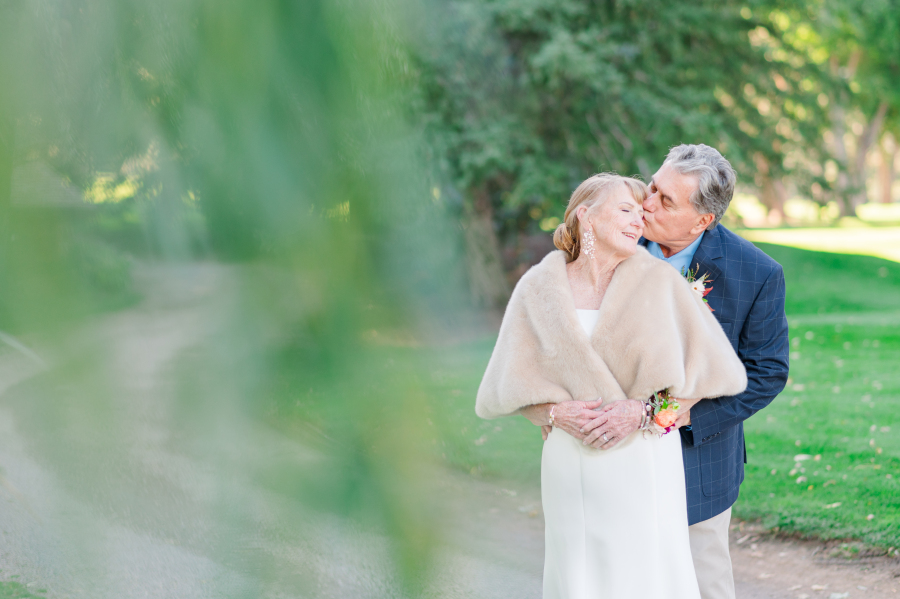A bride leans into a kiss on the forehead from her groom in a blue suit in a path during their broadmoor hotel wedding