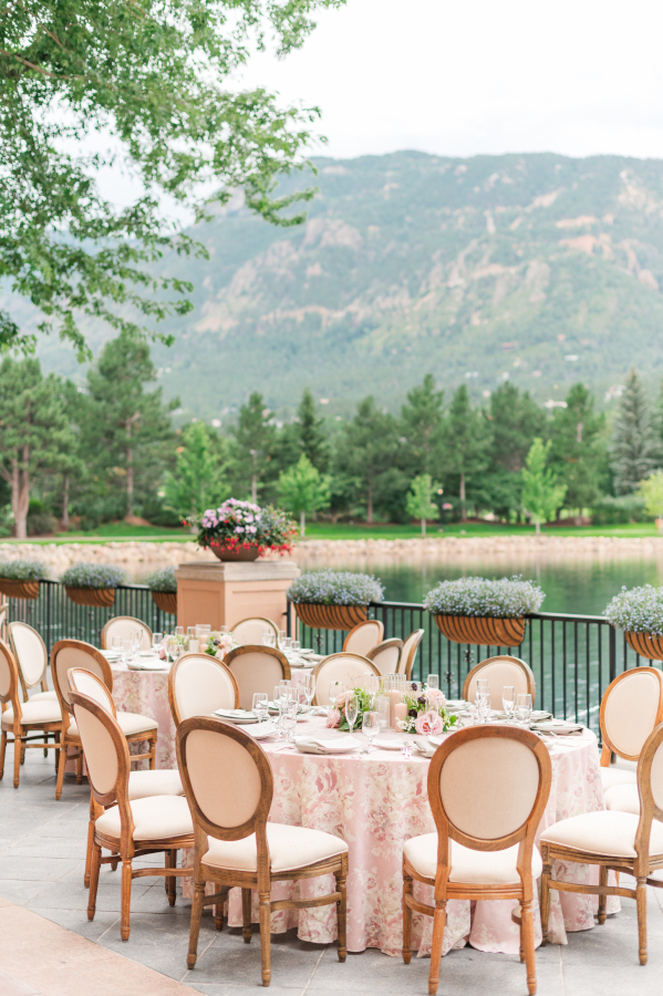Details of an outdoor reception table set up on a waterfront patio with flower print table cloths and wooden chairs at sunset