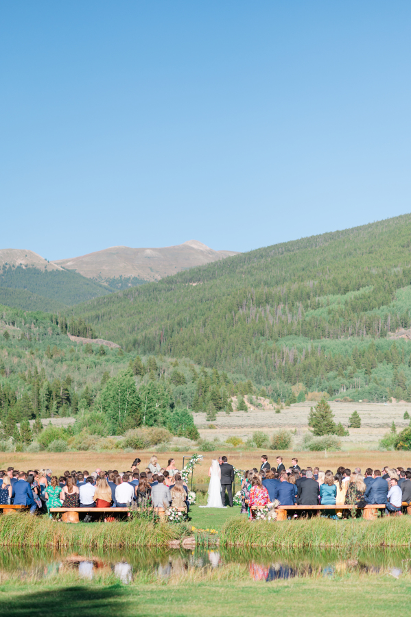 A look across a pond to an outdoor camp hale weddings ceremony in progress on a clear day