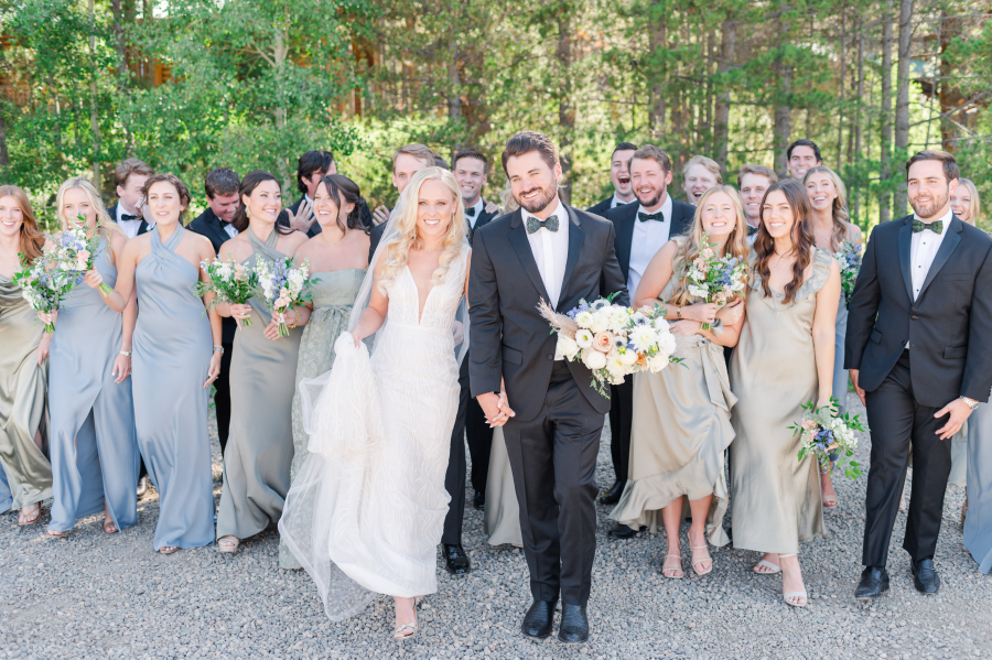 Newlyweds walk holding hands with big smiles in front of their large wedding party