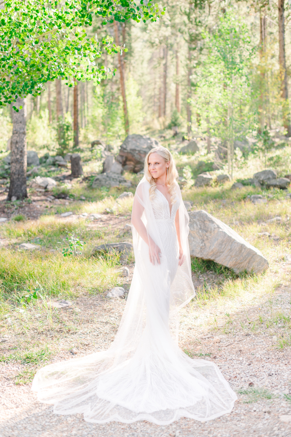 A bride smiles over her shoulder while standing in a forest at camp hale weddings
