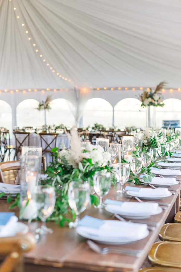 A look down a long wedding reception table lined with greenery under a tent