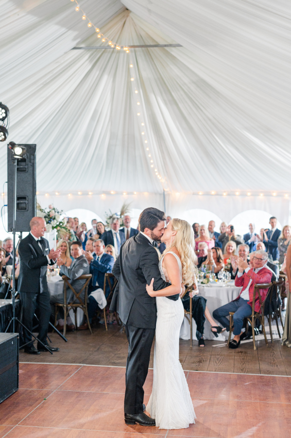A bride and groom share a kiss on the dance floor during their first dance under a reception tent