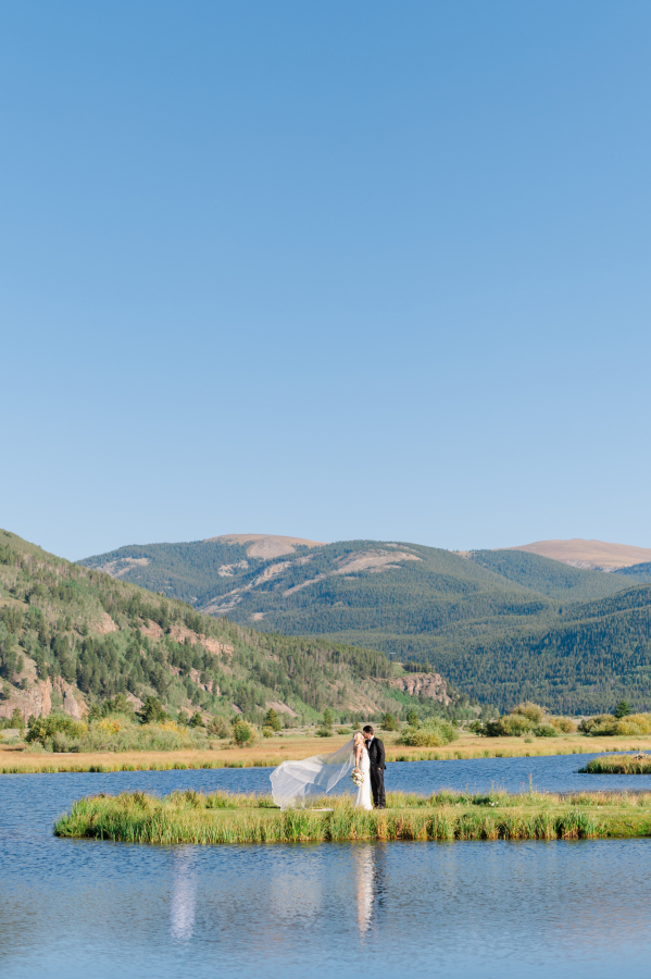 Newlyweds share a kiss on a pond peninsula as the veil flies in the wind
