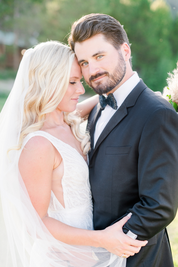 A groom smiles while his bride nuzzles his temple at sunset