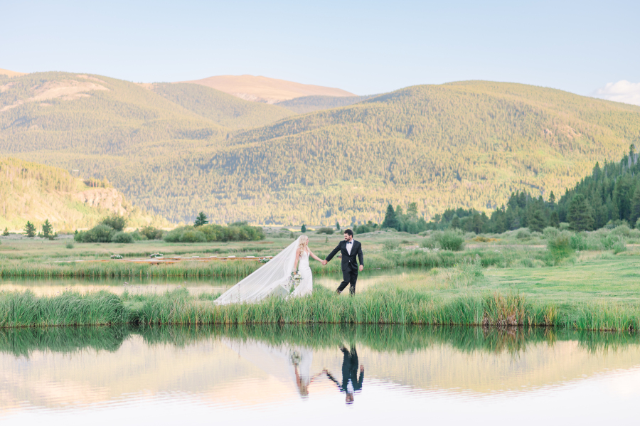 A groom leads his bride by the hands while walking along one of the camp hale weddings venue ponds