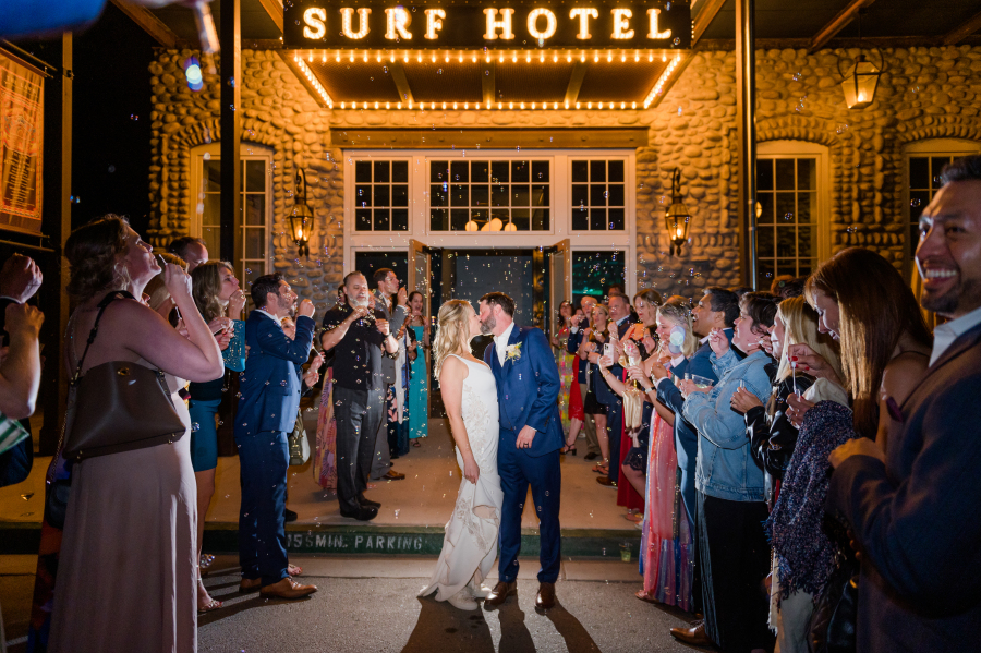 A groom in blue kisses his bride under the surf hotel wedding venue marquee surrounded by bubbles and guests