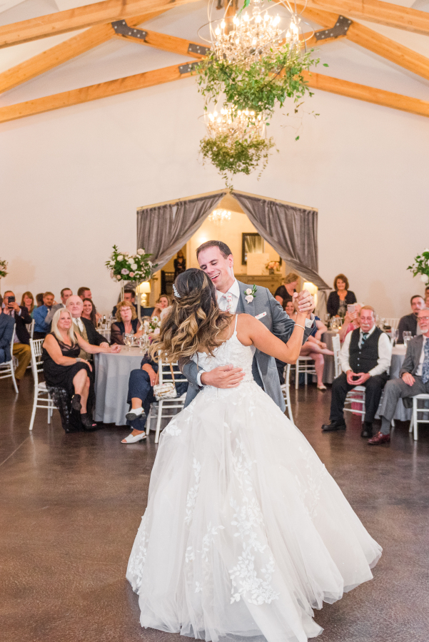 Newlyweds smile big while enjoying a spin during their first dance with guests watching from tables