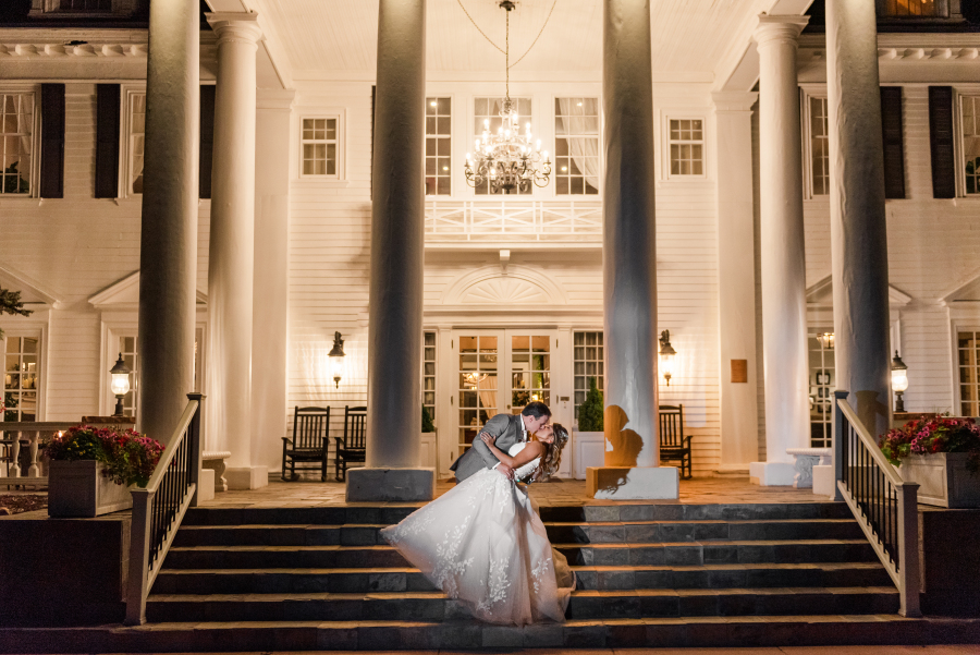 A groom dips his bride on the steps at night under a chandelier for a kiss