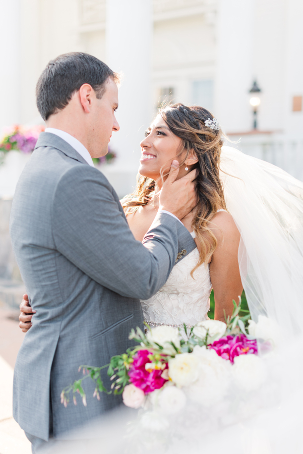 A bride and groom embrace and smile at each other at sunset with the veil flowing around them