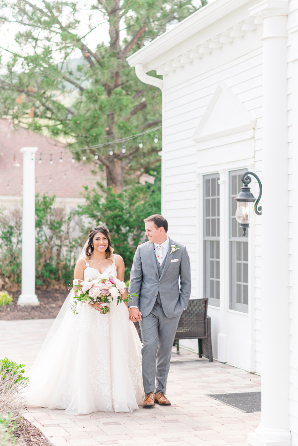 Newlyweds hold hands while smiling, walking, and chatting on a back patio