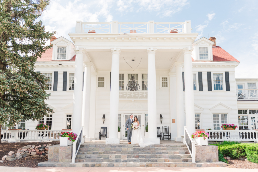 A bride and groom stand together smiling on the front steps of the the manor house wedding venue