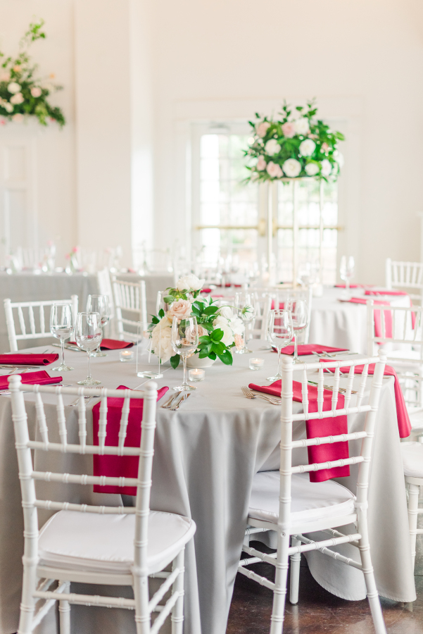 Details of a wedding reception table with white chairs, pink napkins on grey linen and rose centerpieces