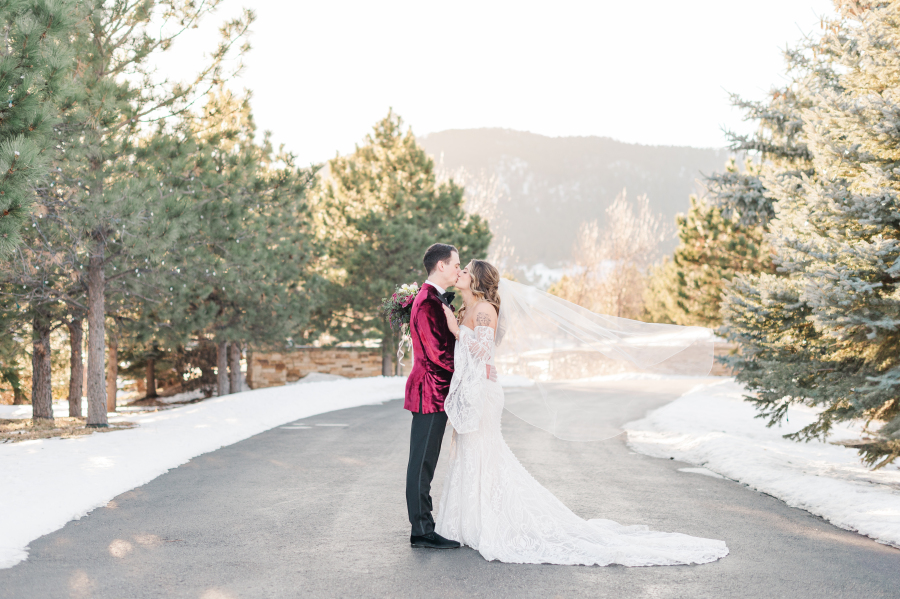 Newlyweds kiss in a snow covered street lined with pines at one of the Colorado Springs wedding venues