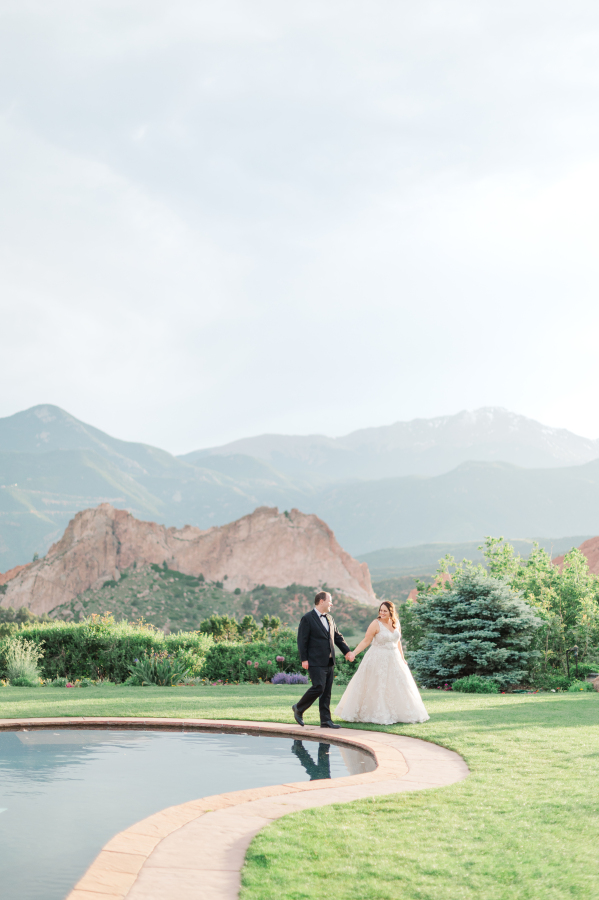 A bride walks leading her groom by the hand around a pond at one of the Colorado Springs wedding venues
