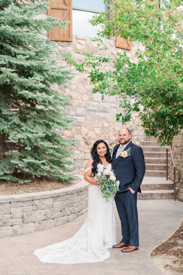 Newlyweds smile while standing together in a garden path lined with stone walls at one of the Colorado Springs wedding venues