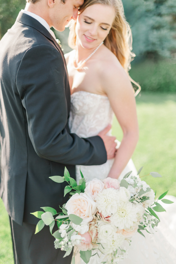 A bride smiles down her shoulder to her white bouquet while snuggling in a lawn with her groomgarden of the gods resort wedding