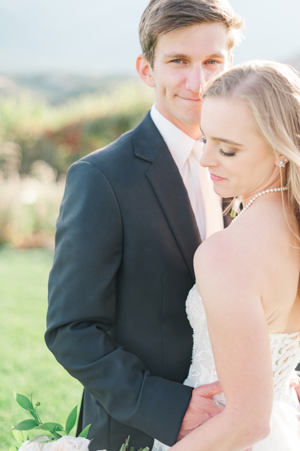 A bride and groom smile while hugging and relaxing in a lawn at sunset during their wedding