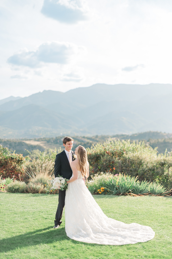 Newlyweds smile at each other while cuddling in the lawn of the garden of the gods resort wedding venue at sunset
