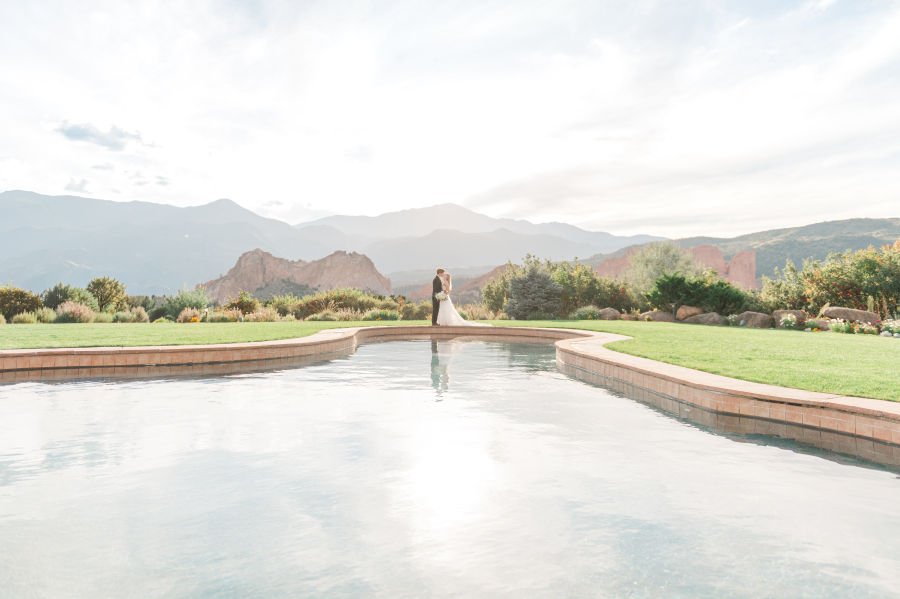 A bride and groom kiss while standing at a pool at sunset
