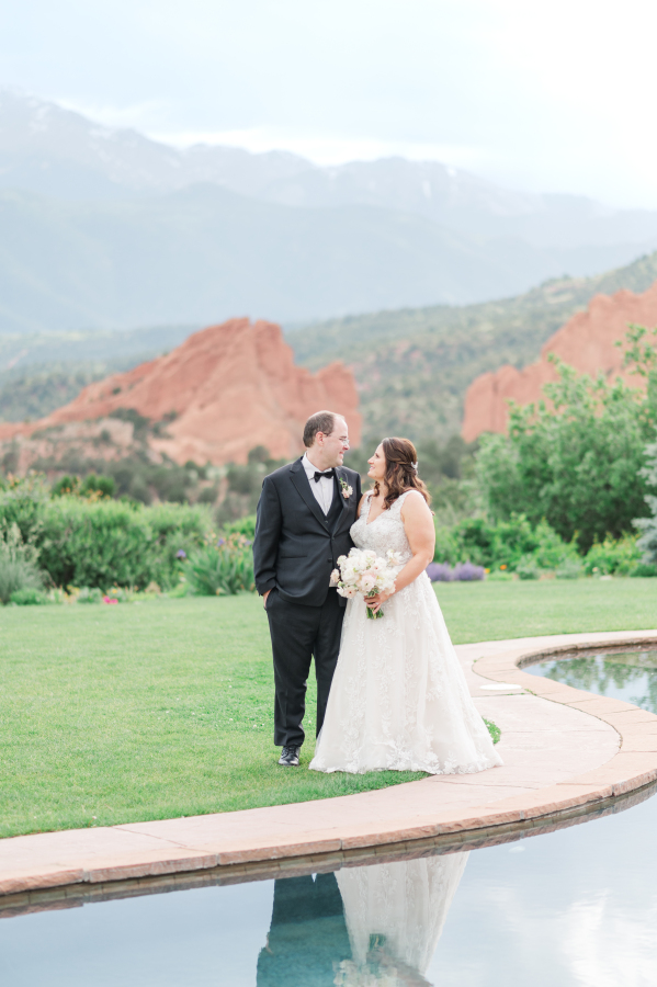 A bride and groom laugh together while standing on the edge of the pool at their epic wedding