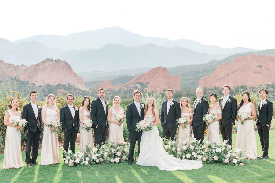 Newlyweds stand smiling with their bridal party and epic view of the garden of the gods resort wedding venue