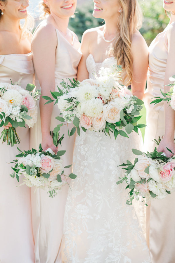 Details of a bride's bouquet as she stands laughing with her bridesmaids in pink
