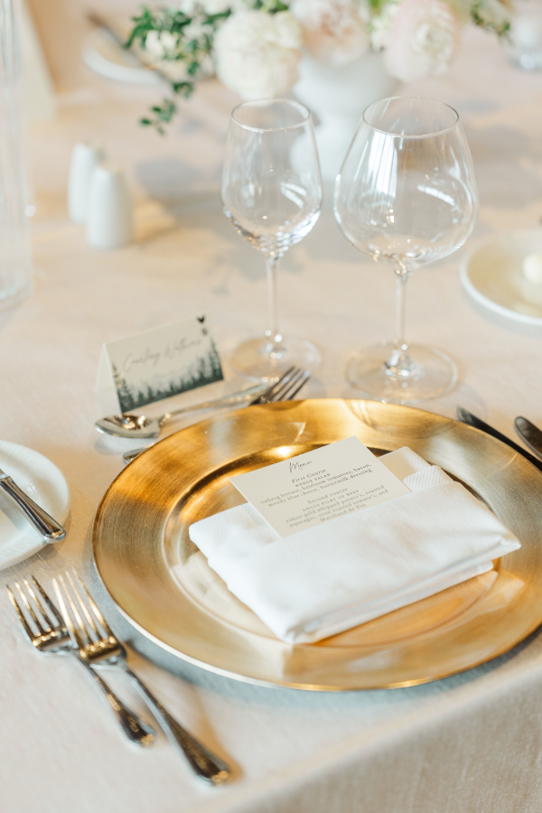 Details of a gold place setting on white linen at a wedding reception