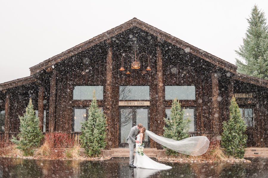 Newlyweds kiss in the snow in front of the spruce mountain ranch wedding venue