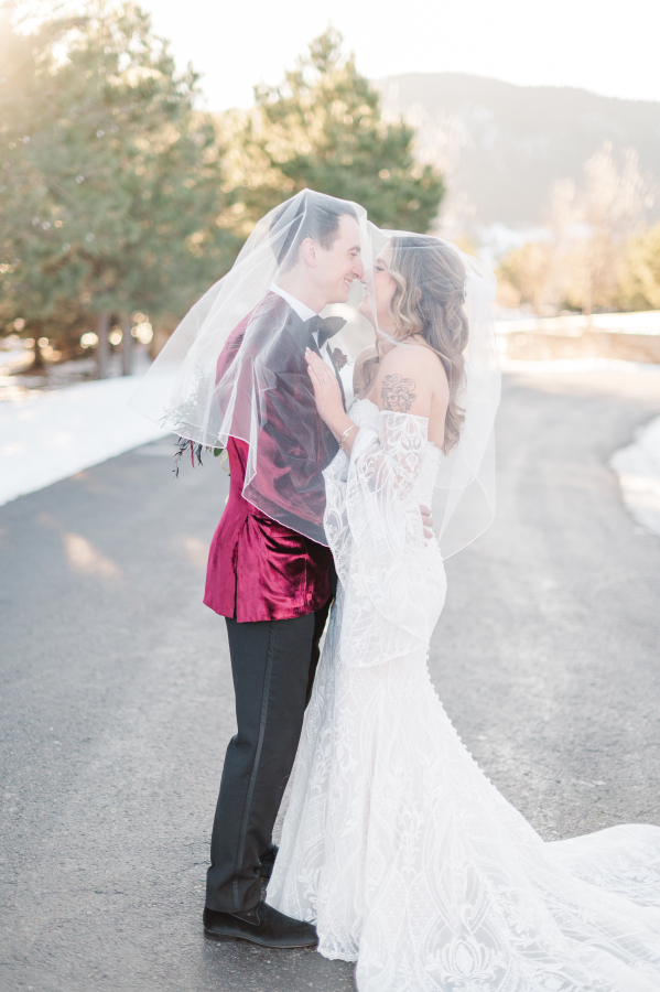 A bride and groom boop noses in a snow lined street at their spruce mountain ranch wedding