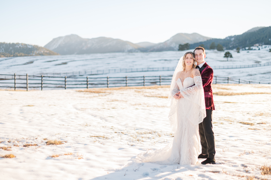 Newlyweds cuddle in a snow covered pasture at sunset during their spruce mountain ranch wedding