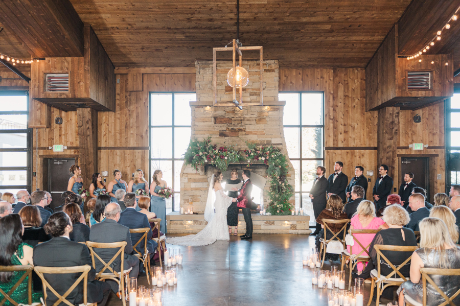Newlyweds stand holding hands at the altar in front of a fireplace covered in florals during their spruce mountain ranch wedding ceremony
