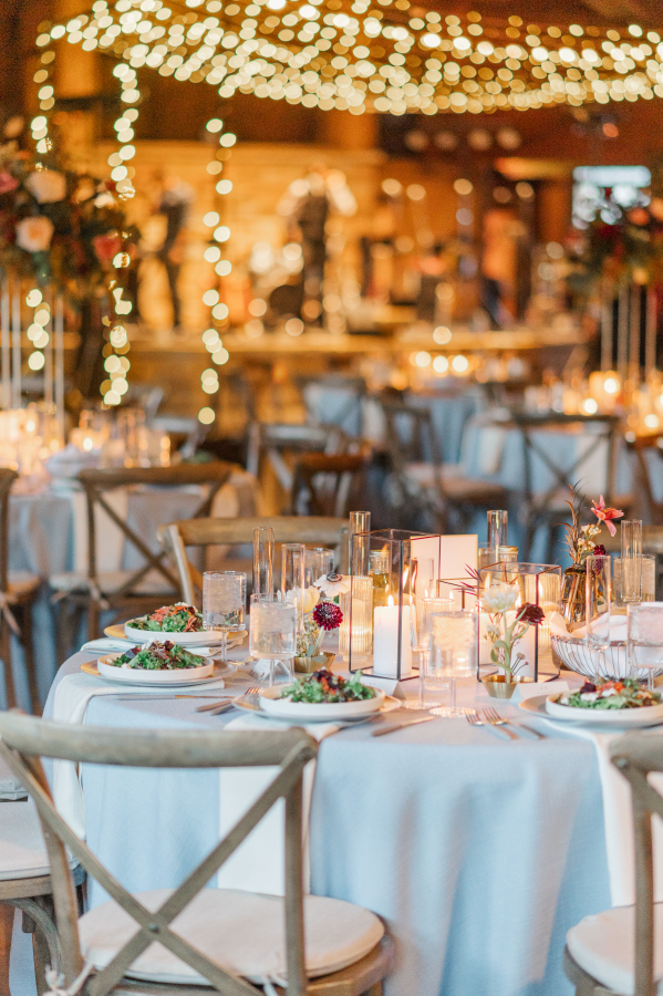 Details of a wedding reception table set up with blue linen under market lights with candles