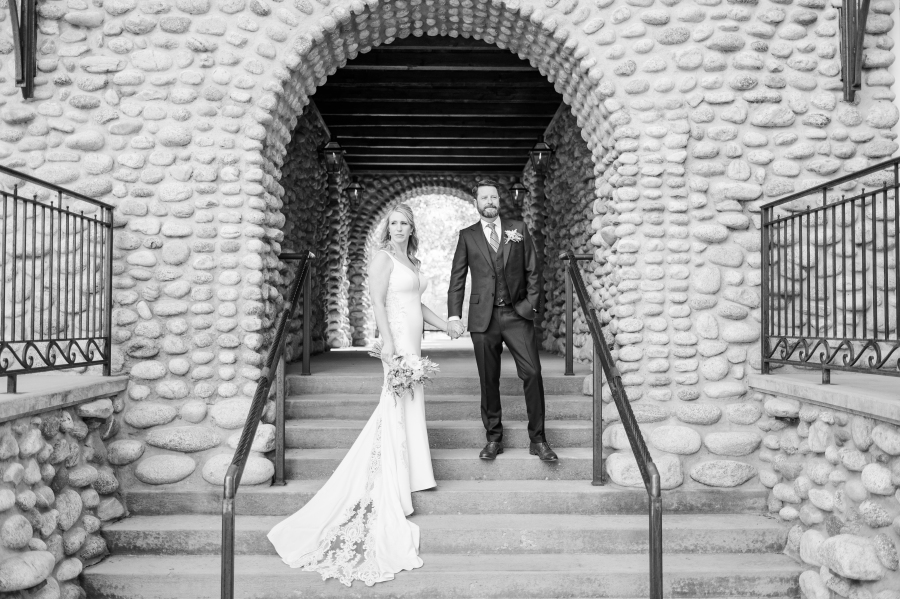 black and white photo of a bride and groom standing on stairs in front of a stone archway at the surf hotel wedding venue