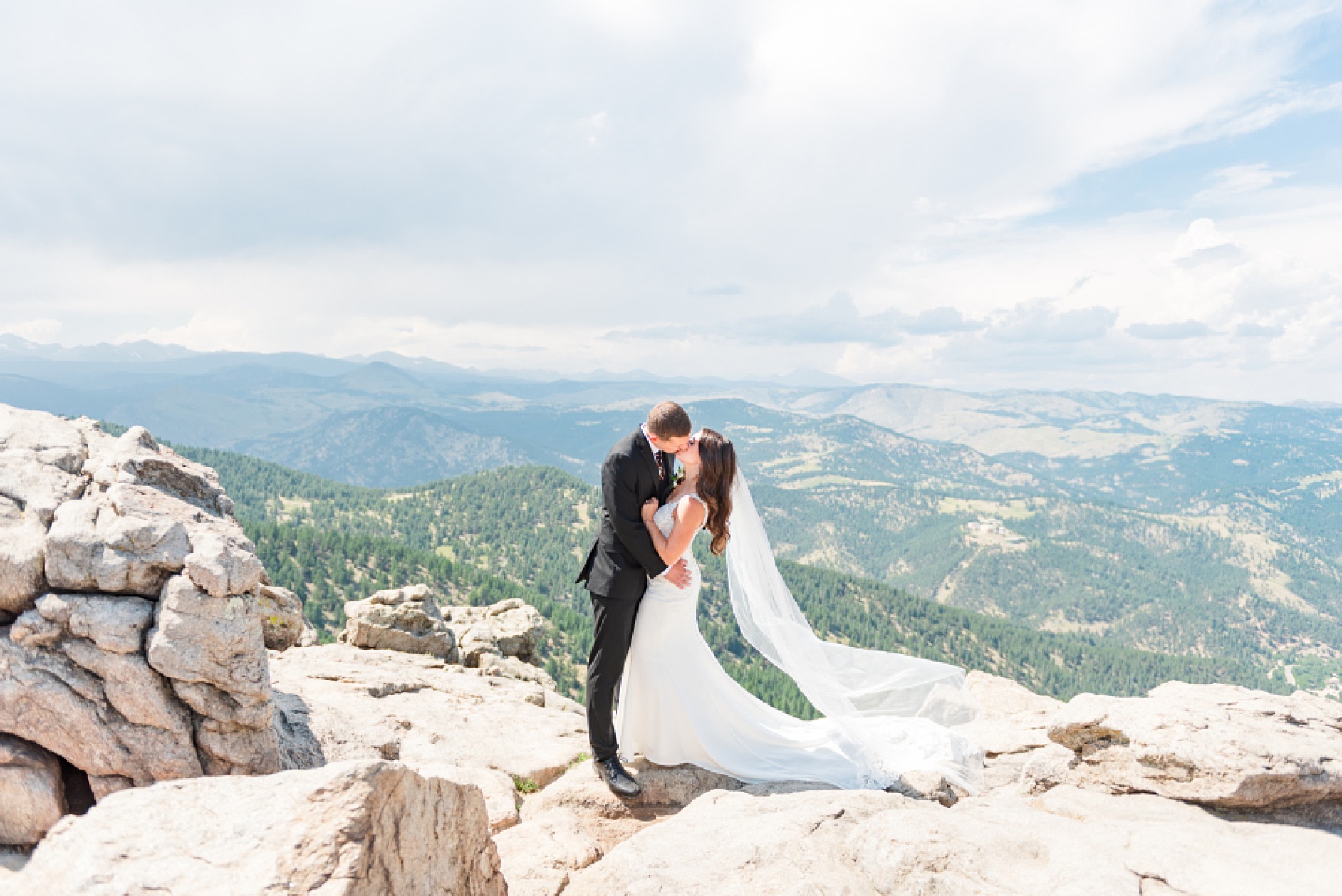 Newlyweds kiss on an epic mountain boulder overlook