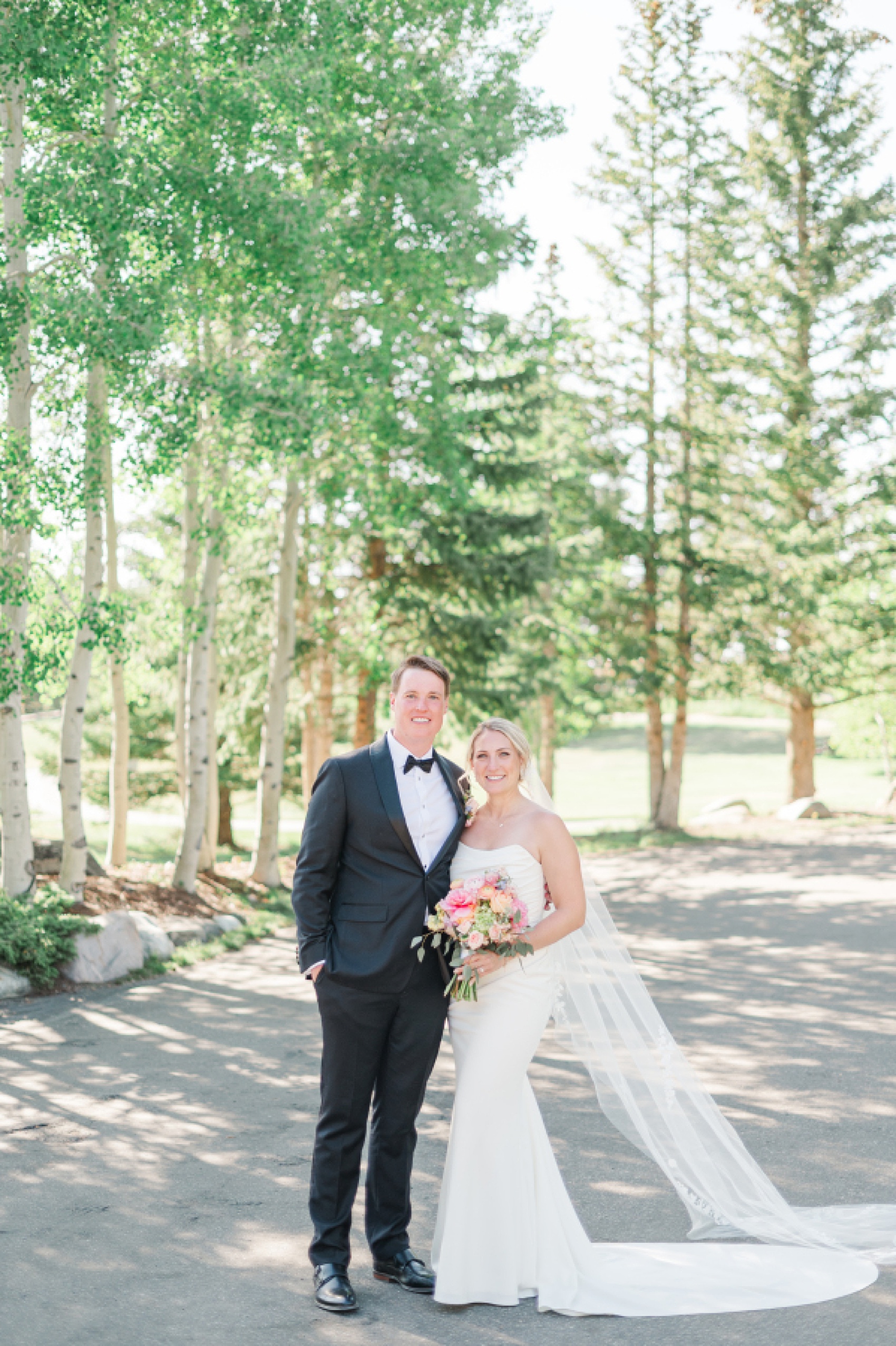 A bride and groom stand smiling with arms around each other in a sidewalk