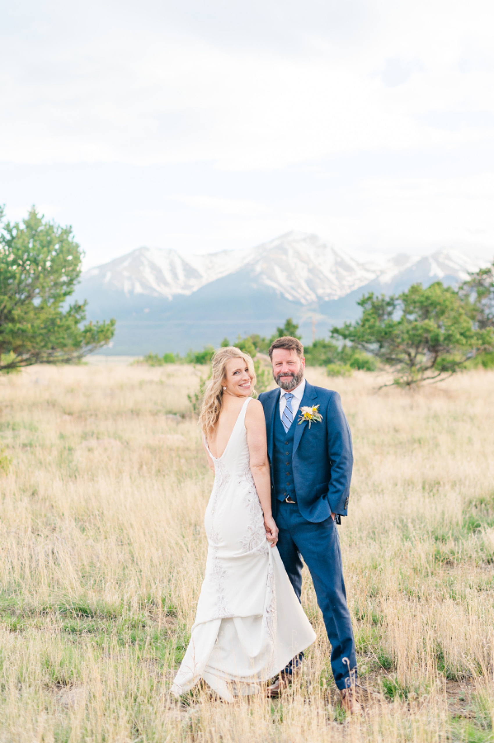 A bride and groom smile and hold hands while snuggling in a meadow at one of the Colorado Mountain Wedding Venues
