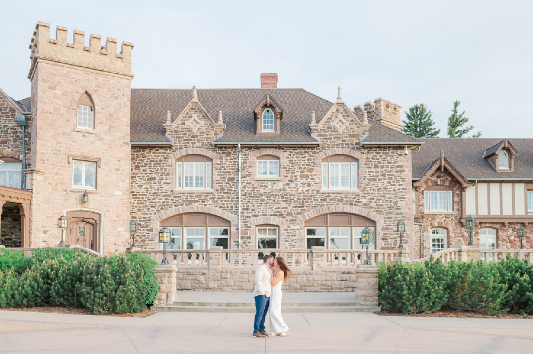 A bride and groom kiss on a patio outside a stone castle style Denver Wedding Venues
